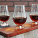A group of Stolzle Glencairn whiskey glasses filled with brown liquid on a wood tray.