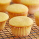 White fluted baking cups filled with yellow cupcakes on a wire rack.