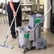 A woman cleaning a floor in a hospital cafeteria with a Unger gray mop bucket.