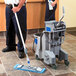 A man and woman using an Unger gray mop bucket and wringer to clean a hospital floor.