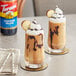 Two milkshakes with whipped cream and chocolate syrup on top in glasses with cookies on the rim.