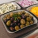 A Vollrath stainless steel food pan filled with olives, cheese, and crackers on a counter.