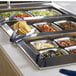 A Vollrath stainless steel food pan on a buffet counter filled with food.