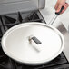 A person holding a Vollrath Wear-Ever fry pan over a stove with a black handle.