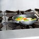 A Vollrath Wear-Ever aluminum non-stick fry pan with a black handle filled with cooking vegetables on a stove.