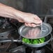 A person cooking broccoli in a Vollrath Wear-Ever non-stick fry pan with a black TriVent handle.