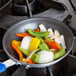 A Vollrath Wear-Ever aluminum non-stick fry pan filled with vegetables on a stove.