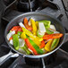 A Vollrath Wear-Ever aluminum non-stick fry pan filled with peppers and onions cooking on a stove.
