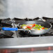 A Vollrath Wear-Ever fry pan with vegetables cooking on a stovetop.