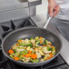A person cooking vegetables in a Vollrath Wear-Ever non-stick fry pan.