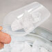 A hand using a Fineline clear plastic utility and ice scoop to scoop ice cubes.