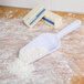 A white plastic scoop with white flour on a wooden surface.