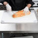 A person cutting bread with a knife on a San Jamar color-coded cutting board.