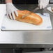 A person using a knife to cut bread on a San Jamar color-coded cutting board.