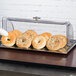 A Tablecraft rectangular polycarbonate roll top lid on a table of bagels.
