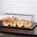 A hand putting bagels into a Tablecraft rectangular polycarbonate roll top lid on a counter.