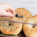 A hand using a metal Tablecraft lid to cover a bagel on a counter.
