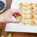 A hand holding a 10 Strawberry Street white porcelain square platter with mini pastries.