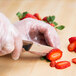 A person in gloves using a Mercer Culinary Millennia Colors brown paring knife to cut a strawberry.