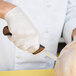 A hand in a white glove using a Mercer Culinary Millennia Colors narrow boning knife with a brown handle to cut turkey.
