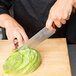 A person holding a Mercer Culinary Millennia Colors chef knife with a brown handle and cutting a lettuce leaf.
