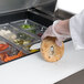 A hand in a glove placing a bagel in a food container on a Traulsen sandwich prep table.