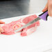 A person using a Mercer Culinary purple boning knife to cut meat on a cutting board.