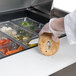 A person using a Traulsen refrigerated sandwich prep table to make a bagel sandwich.