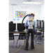 A person using a ProTeam Super CoachVac backpack vacuum cleaner in a classroom.