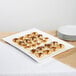 A 10 Strawberry Street Whittier white porcelain rectangular platter with food on a table.