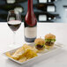 A rectangular white porcelain platter with burgers and chips next to a glass of red wine.