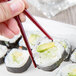 A hand holding a sushi roll with 10 Strawberry Street Whittier bamboo chopsticks.