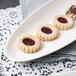 A white 10 Strawberry Street oval leaf platter with three cookies, each with jam on top.