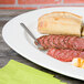 A 10 Strawberry Street white porcelain oval platter with slices of meat, a bread roll, and a knife on a table.