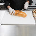 A person in a white apron using a San Jamar white cutting board to cut a loaf of bread with a knife.