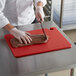 A chef cutting meat on a red San Jamar cutting board.