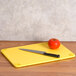 A San Jamar yellow cutting board with a knife cutting a tomato.