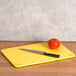 A yellow San Jamar cutting board with a knife and tomato on it.
