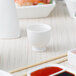 A white bowl with red sauce and chopsticks on a table with a white 10 Strawberry Street Whittier sake cup.