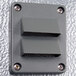 A grey rectangular Kolpak wall plate with metal corners and two holes.
