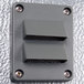 A gray rectangular wall plate with metal corners and two holes.