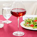 A Stolzle Quatrophil burgundy wine glass filled with red wine sits on a table next to a plate of salad.