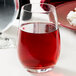 A Stolzle stemless wine glass filled with red liquid sits on a table.