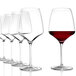 A row of six Stolzle burgundy wine glasses filled with red wine.