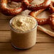 A pretzel with Regal Yellow Mustard dip on a table with a jar of mustard and pretzels.