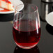 A Stolzle stemless wine glass filled with red wine on a table.