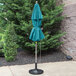A turquoise Grosfillex Windmaster umbrella on a pole on a concrete patio.