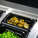 A Vollrath 1/9 size black polycarbonate food pan filled with peas and green beans on a counter.