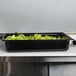 A Vollrath black polycarbonate food pan with lettuce in it.