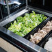 A Vollrath black polycarbonate food pan filled with chicken, lettuce, and other vegetables on a buffet counter.